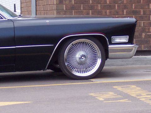 1972 Ford Ranchero - Side view of a black car chrome wire wheels and a chrome bumper against a brick wall.