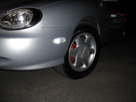 1999 Ford Taurus - The front quarter panel and wheel of a silver 1999 Ford Taurus are visible in this close-up shot.