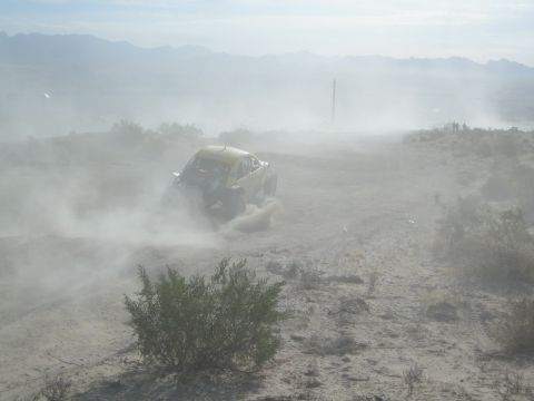 Off-road race car partly obscured by thick dust on a desert hillside