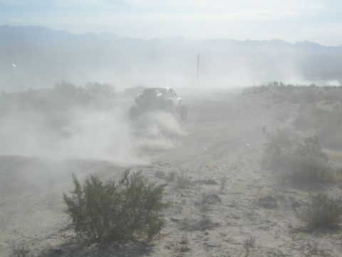 Off-road race buggy shrouded in dust racing across an open desert plain