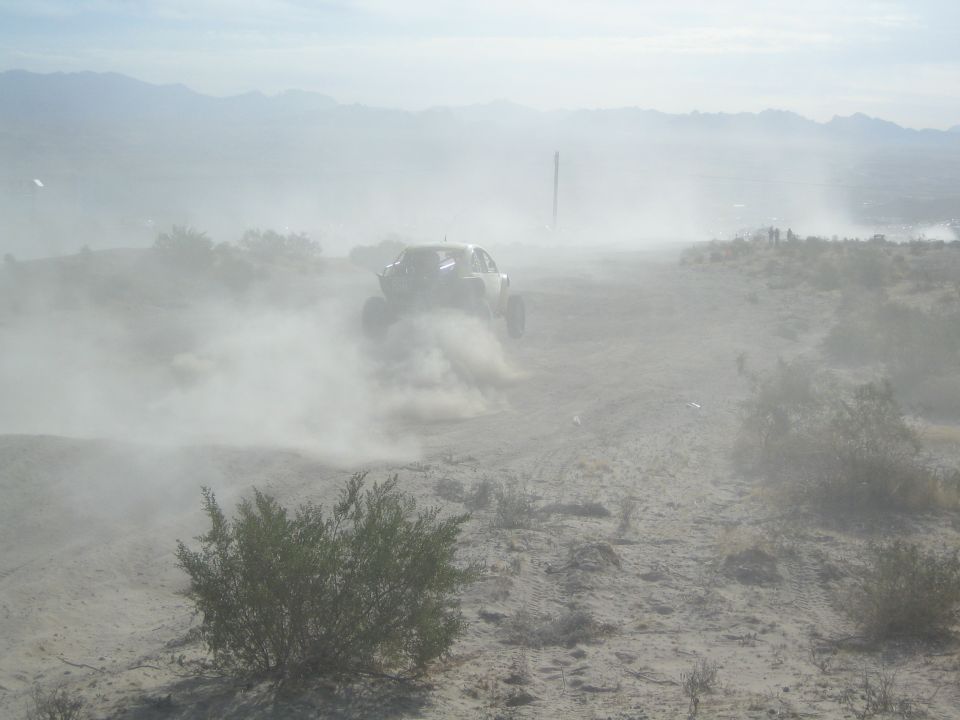 Off-road race buggy shrouded in dust racing across an open desert plain