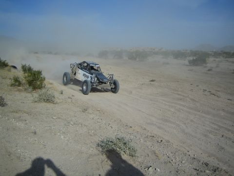 Open-frame off-road race buggy racing across a sandy desert wash