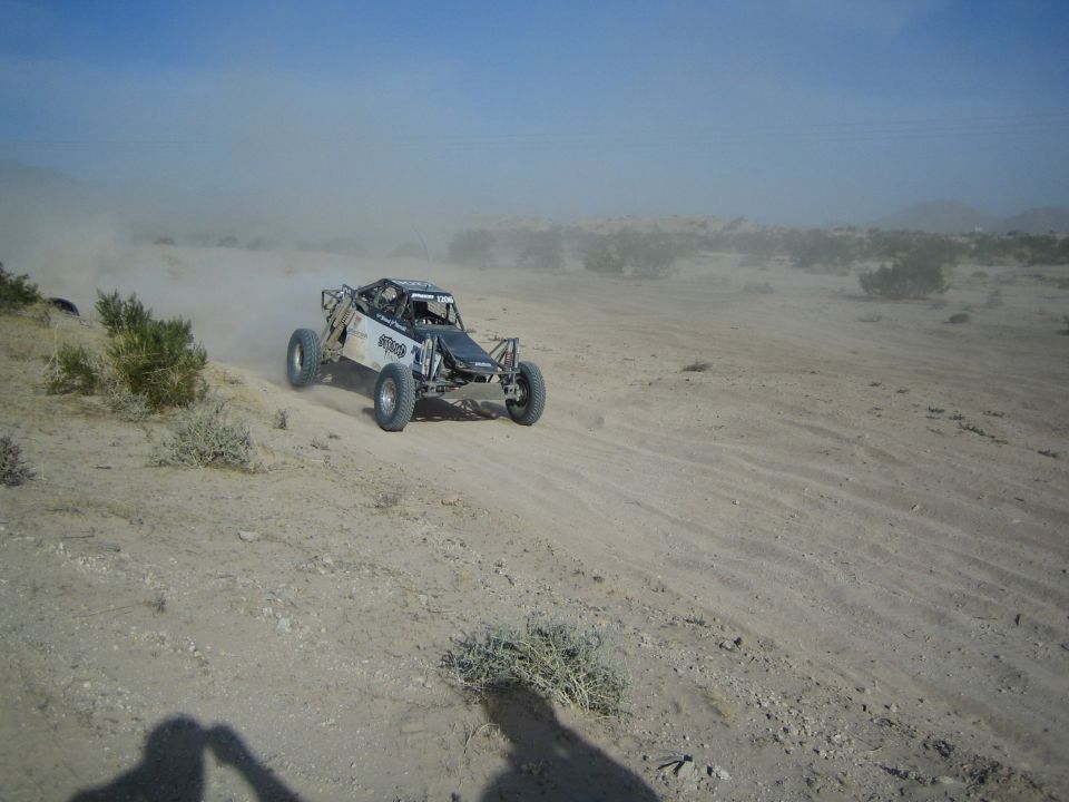 Open-frame off-road race buggy racing across a sandy desert wash