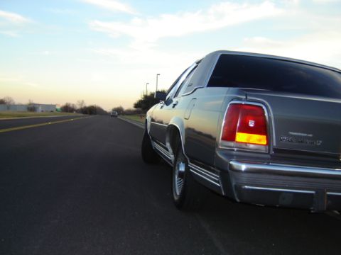 1988 Ford Crown Victoria LTD - Rear view of a gray 1988 Ford Crown Victoria LTD driving on a highway at dusk.