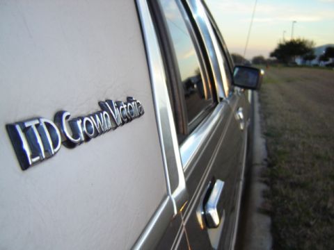 1988 Ford LTD Crown Victoria - The LTD Crown Victoria badge is visible on the side of the car, with chrome accents and a view of the road ahead.