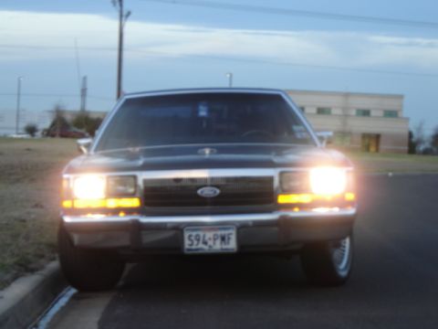 1988 Ford LTD Crown Victoria - Front view of a black 1988 Ford Crown Victoria LTD with its headlights illuminated.