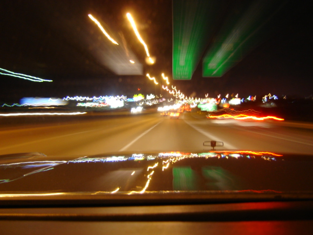 Dashboard view of highway lights at night with a reflection on the hood