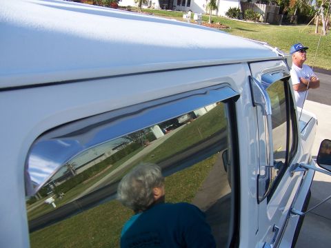 1993 Ford C-350 (Centurion Conversions) - Chrome vent shades are installed on the side window of a white van, with two people nearby.