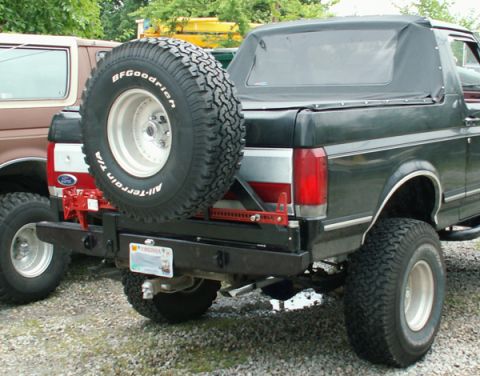 1988 Ford Bronco - Rear view of a dark green Ford Bronco with a spare tire and custom bumper, alongside another vehicle.