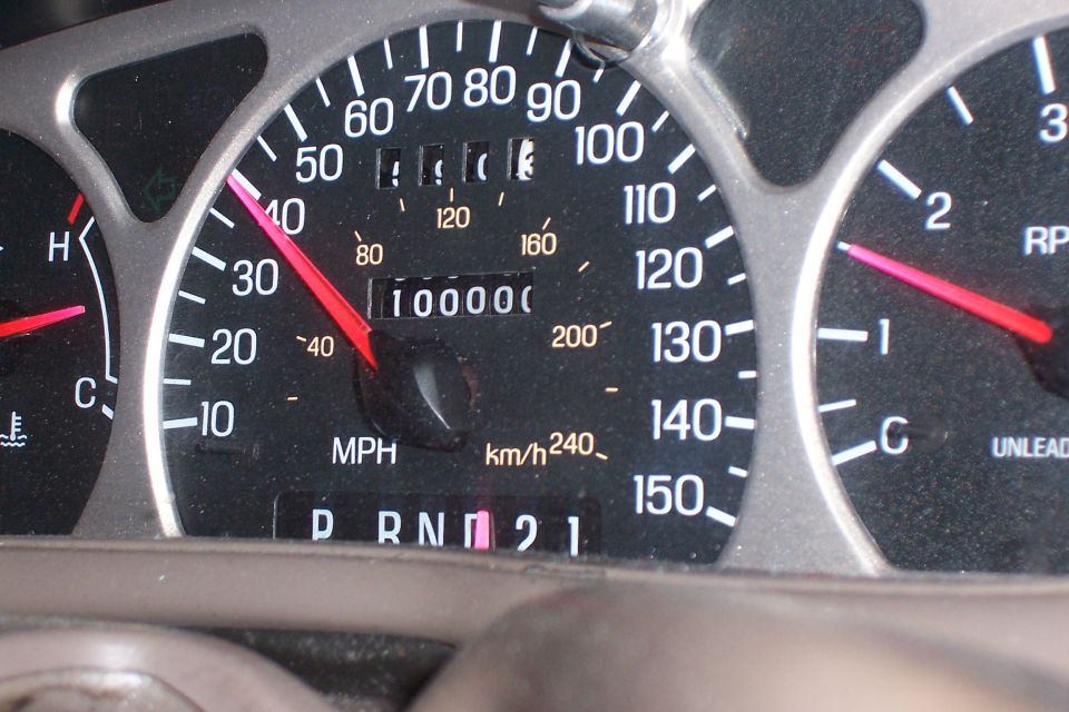 Car dashboard showing odometer at 100,000 miles, speedometer needle near 35 mph, and tachometer needle near 1000 RPM