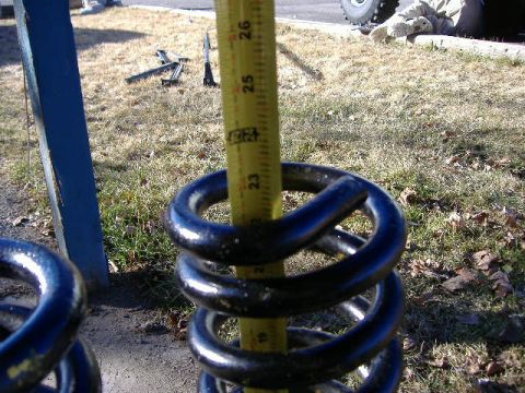 1979 Ford Bronco - A yellow measuring tape is used to measure the height of black coil springs.