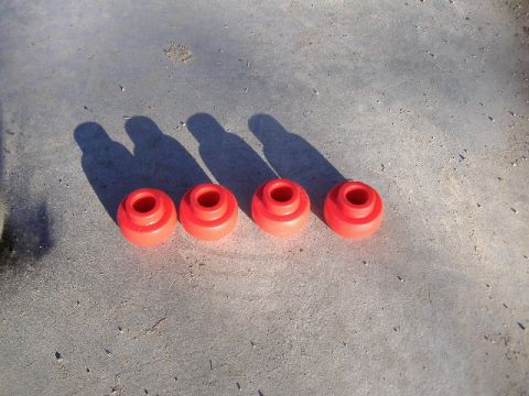 1979 Ford Bronco - A set of four red suspension bushings are laid out on a concrete surface, casting long shadows.