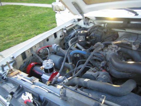 1990 Ford Bronco - open engine bay of a white vehicle, viewed under a raised hood, showing hoses, an air compressor and the radiator support.