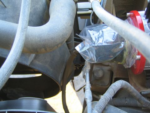 1990 Ford Bronco - Dusty engine bay hoses with a small component in a plastic bag and the edge of a red compressor visible at right.