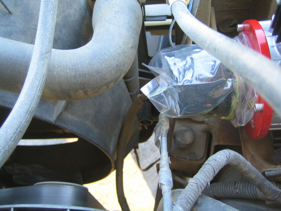 Engine bay hoses and a small bagged component near a red compressor