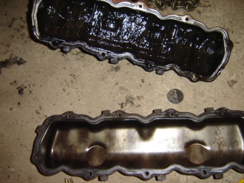 1992 Ford Bronco - Two engine valve covers, one heavily coated in sludge, are shown on a concrete surface.