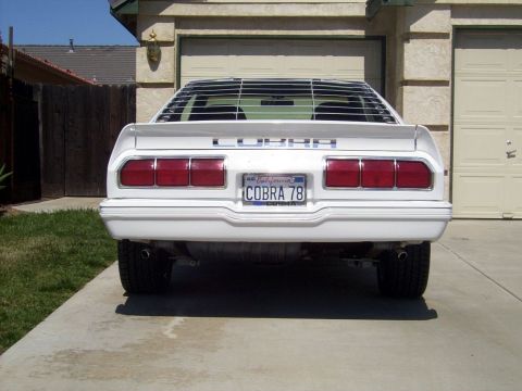 1978 Ford Mustang II - The rear of a white 1978 Ford Mustang II Cobra is shown parked in a driveway, distinctive horizontal louvers on the back window.