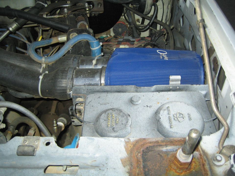 Blue cylindrical component mounted on an aluminum bracket in an engine bay