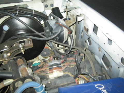 1990 Ford Bronco - largely stripped engine bay showing the firewall, brake booster, exposed wiring harness and a blue component at bottom.