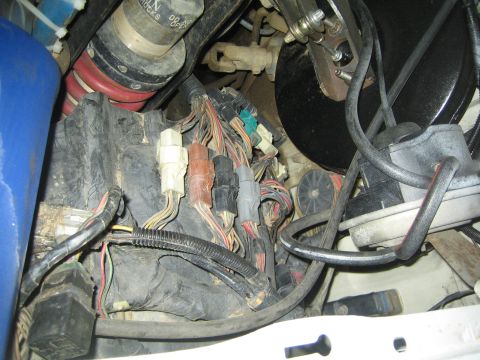 1990 Ford Bronco - cluster of multi-pin wiring connectors and a worn harness sit exposed in a dirty engine bay near the brake booster.