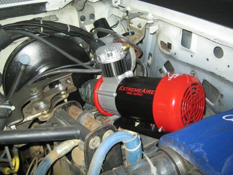 1990 Ford Bronco - red and silver ExtremeAire High Output air compressor is bolted into an engine bay above hoses and a blue component.