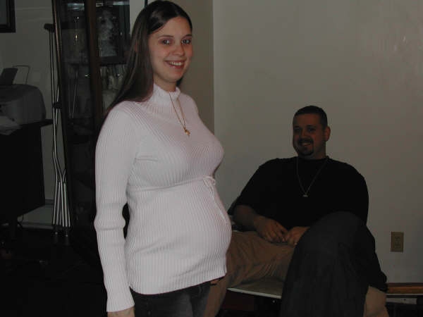Woman in white sweater standing indoors with a seated man smiling in the background