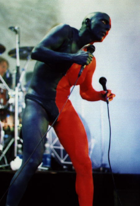1991 Ford Bronco - Performer on stage with blue and red body paint, holding microphones.