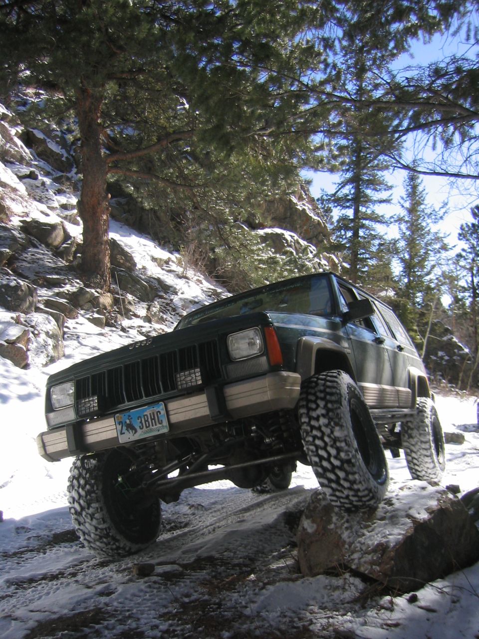 Dark green 1997 Jeep Cherokee off-roading on a snowy, rocky trail