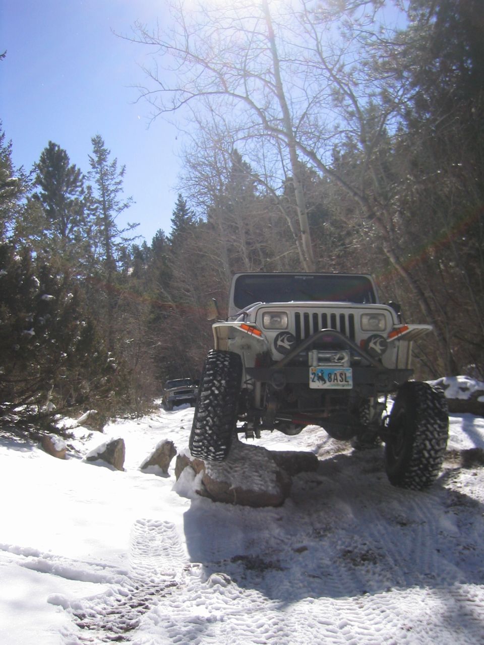 White lifted Jeep Wrangler YJ with winch bumper climbing a rock on a snowy trail, front view