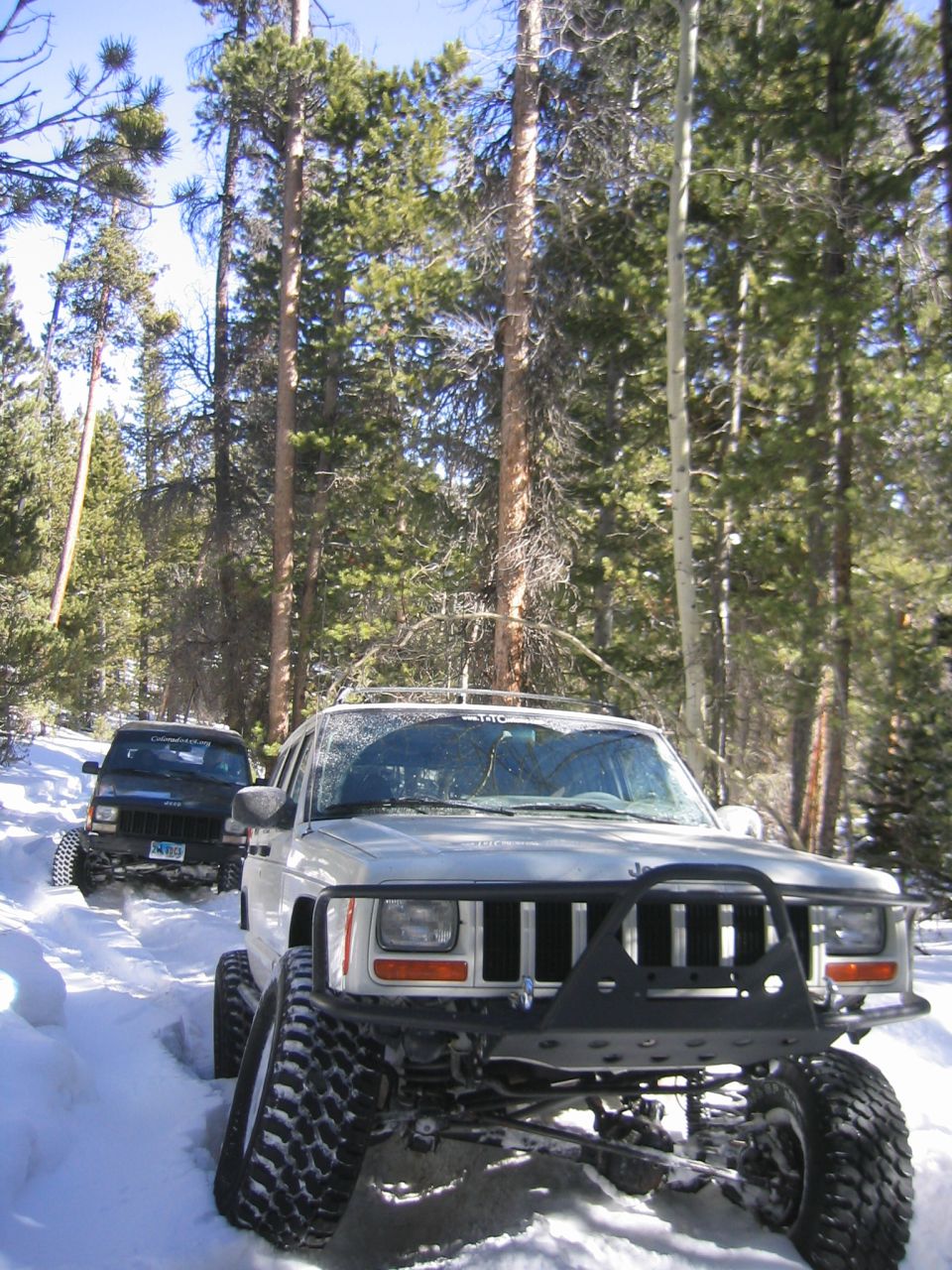 Silver 1997 Jeep Cherokee with aftermarket bumper and large tires in snow