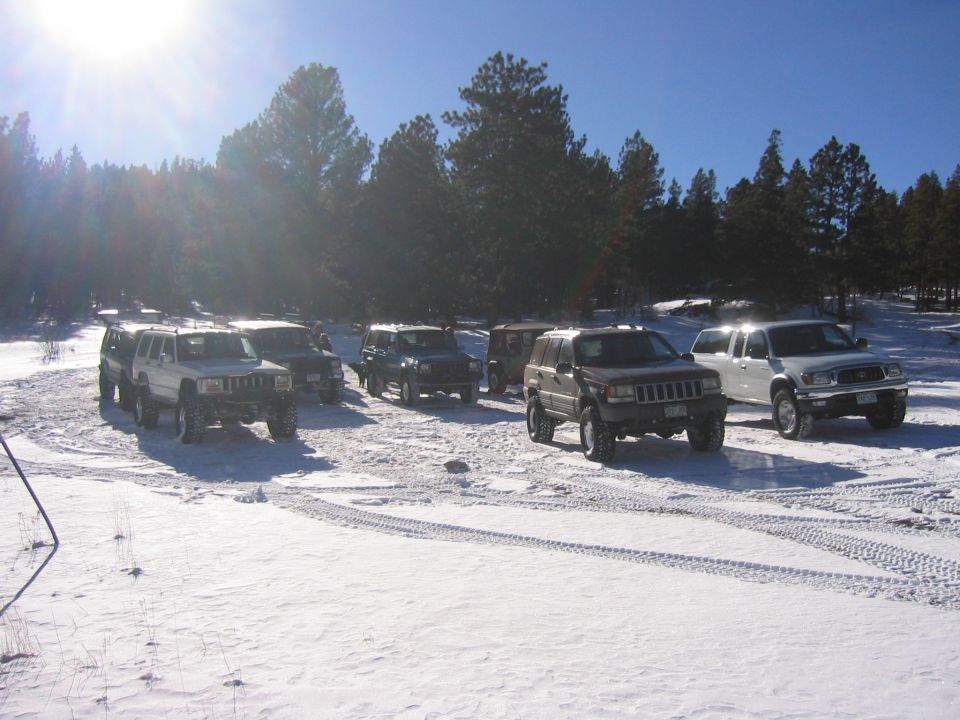Several Jeep Cherokees and a Toyota Tacoma parked in a snowy forest clearing