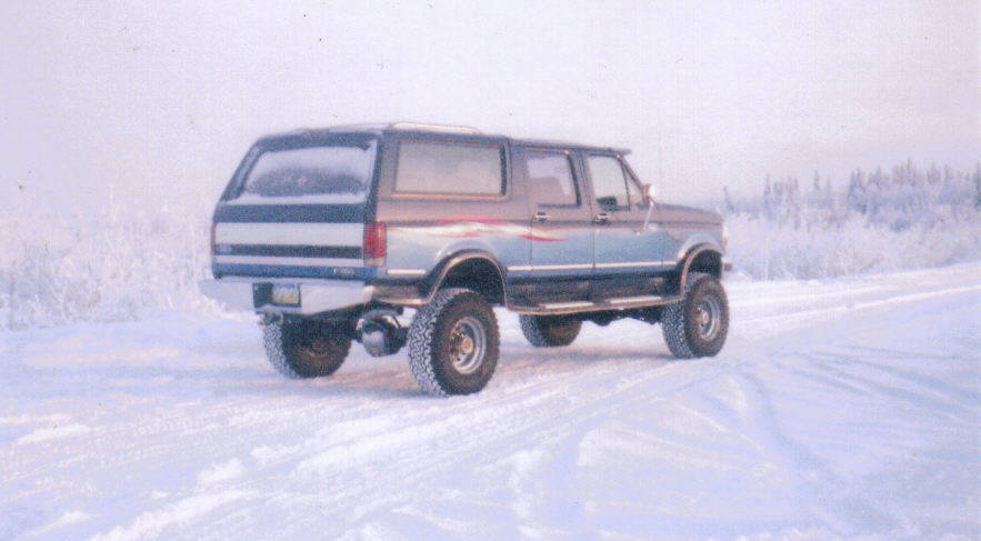 Blue lifted extended SUV parked on snowy road, rear 3/4 view