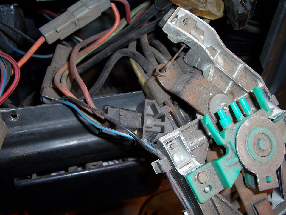 Close-up of a vehicle's underdash wiring harness with connectors and a green plastic component