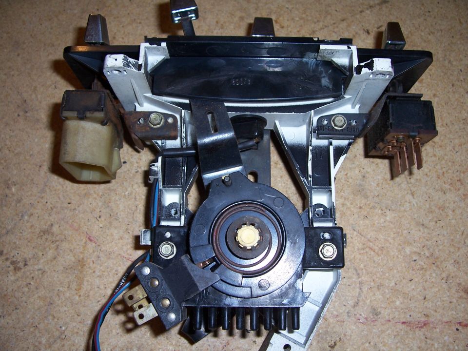 Automotive dashboard component with wiring and mechanical linkages, showing a black plastic housing with metal brackets and electrical connectors