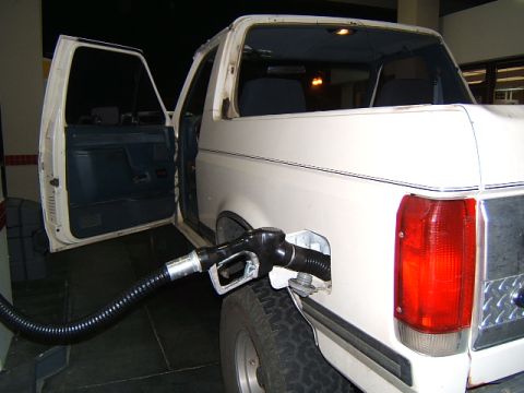 1988 Ford Bronco - A white SUV is being refueled at a gas station, with the driver's side door open.
