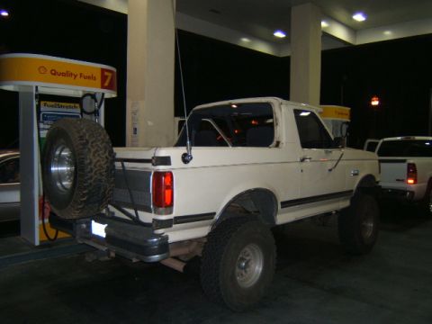 1988 Ford Bronco - A white 1988 Ford Bronco is parked at a gas station with a spare tire mounted on the rear bumper.