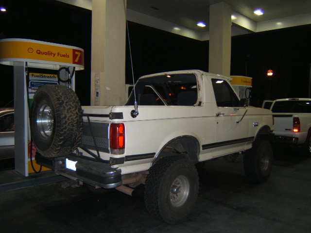 White 1988 Ford Bronco with spare tire on rear bumper at gas station