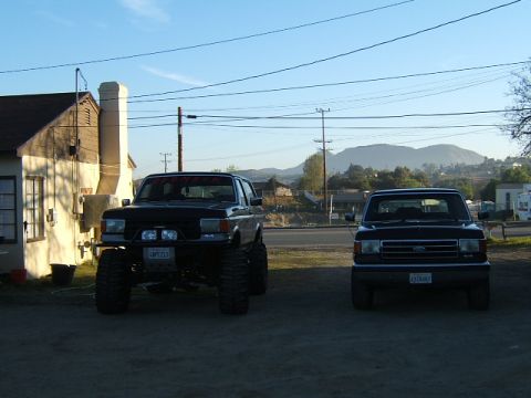 1988 Ford Bronco - Two Ford trucks, a Bronco and an F-150, are parked side-by-side in a lot.