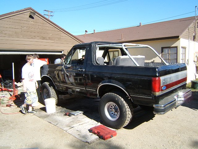 Black Ford Bronco with roll cage, parked outside a garage with people around