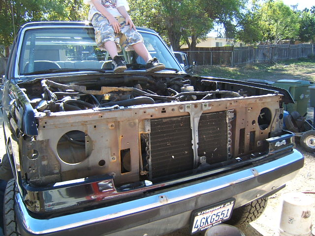 Black Ford Bronco with front end disassembled, showing radiator and engine components. A person sits on the hood