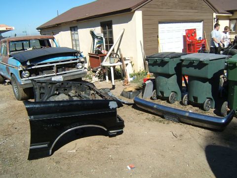 1988 Ford Bronco - A disassembled truck sits in a yard with a detached fender and bumper in the foreground.