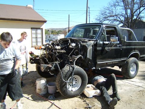 1988 Ford Bronco - A black 1988 Ford Bronco is shown with its front end disassembled while mechanics work on it.