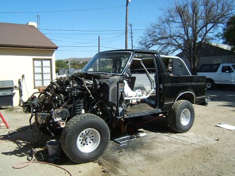 1988 Ford Bronco - A black Ford Bronco is shown partially disassembled with its engine compartment empty and a roll cage visible inside.