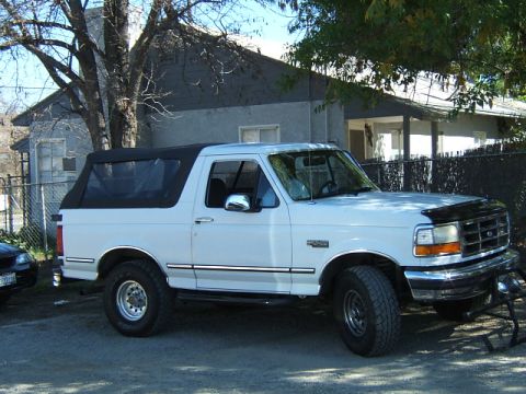 1988 Ford Bronco - White Ford Bronco with a black soft top is parked in front of a house.