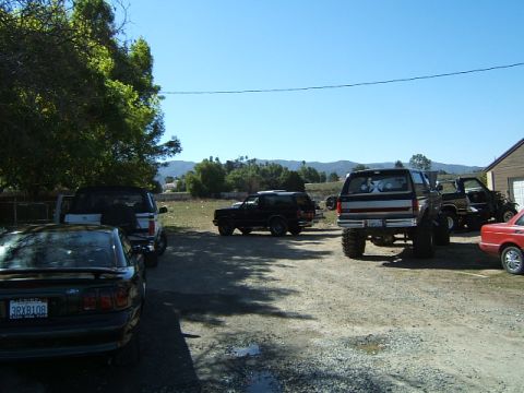 1988 Ford Bronco - Several vehicles, including a 1988 Ford Bronco, are parked in a lot on a sunny day.
