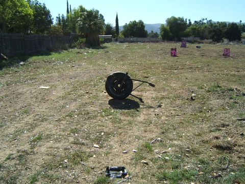 1988 Ford Bronco - A spare tire and jack are discarded in an open, dry field with scattered debris and distant trees.