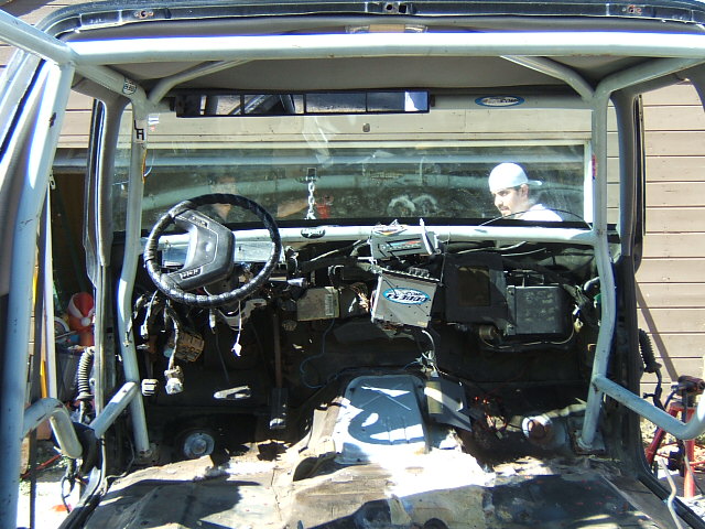 Interior of a vehicle with a roll cage, exposed dashboard, and a person in the background