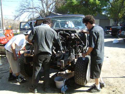 1988 Ford Bronco - Three men work on a Ford Bronco with its engine disassembled in an outdoor repair area.
