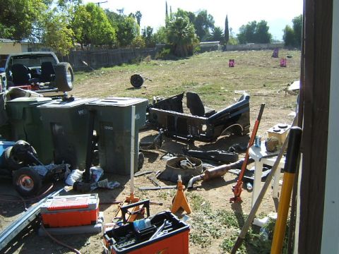 1988 Ford Bronco - A disassembled vehicle body and various parts are visible in a yard, surrounded by trash cans and tools.