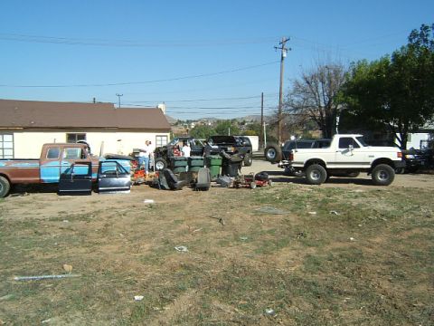 1988 Ford Bronco - Yard scene with a white Ford Bronco, a disassembled pickup truck, and various automotive parts.